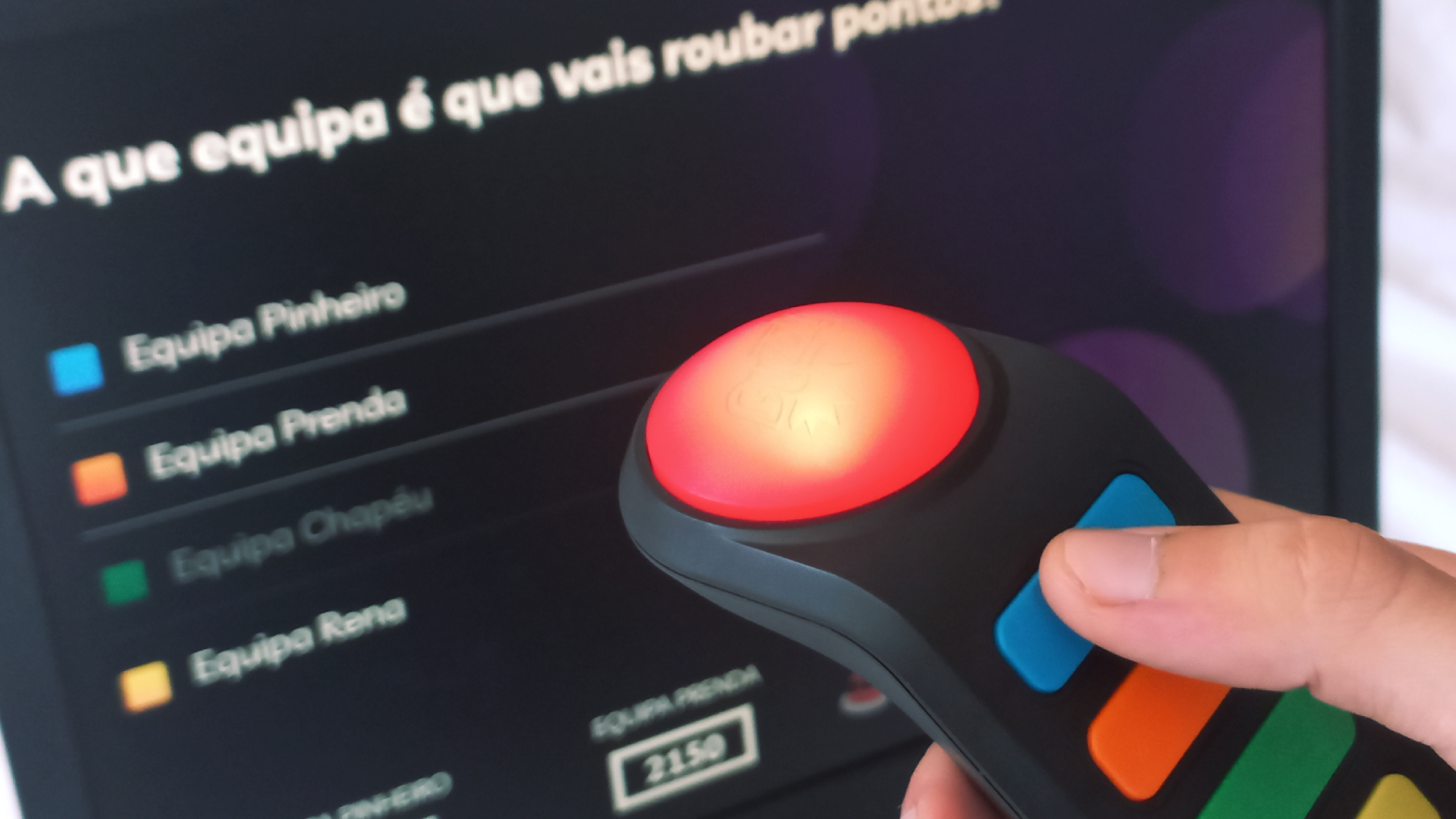 Alguém a segurar uma campainha Buzz&trade; em frente a um ecrã de jogo.